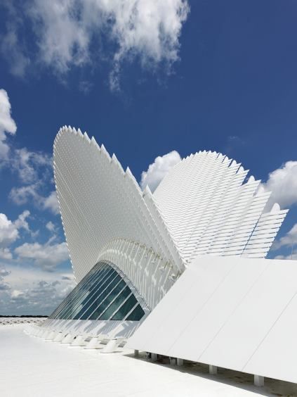 a large white building sitting under a blue sky with some clouds in the background on a sunny day