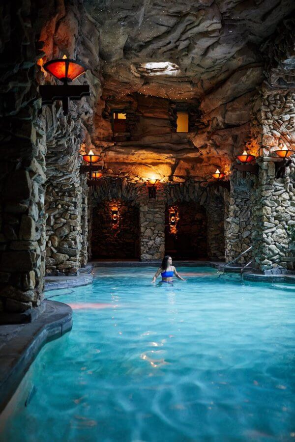 a woman sitting in the middle of a pool surrounded by stone walls and lamps on either side