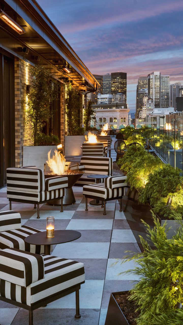 an outdoor seating area with black and white striped chairs, fire pit and cityscape in the background