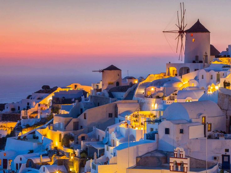 the white buildings are lit up with lights on them at sunset or dawn in oia