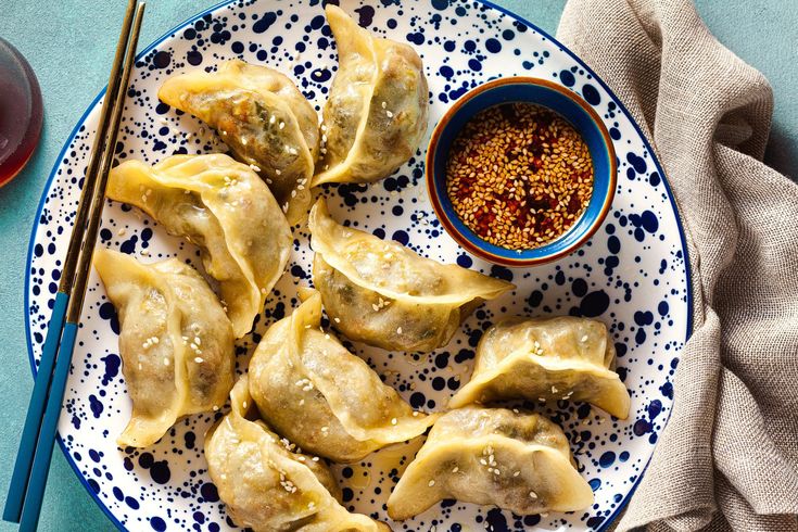 some dumplings are on a blue and white plate with chopsticks next to it