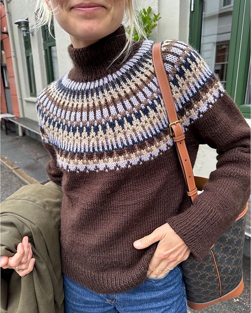 a woman with blonde hair wearing a brown sweater and holding a bag in her hands