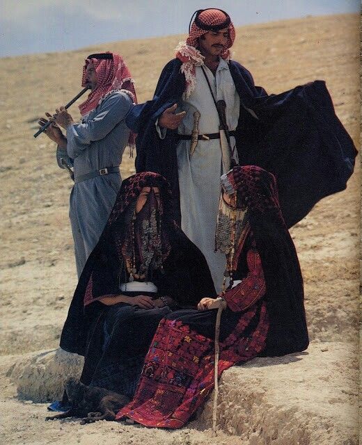 three people dressed in traditional clothing standing on the beach