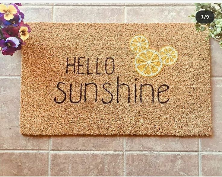 a door mat with the words hello sunshine written on it next to purple pansies