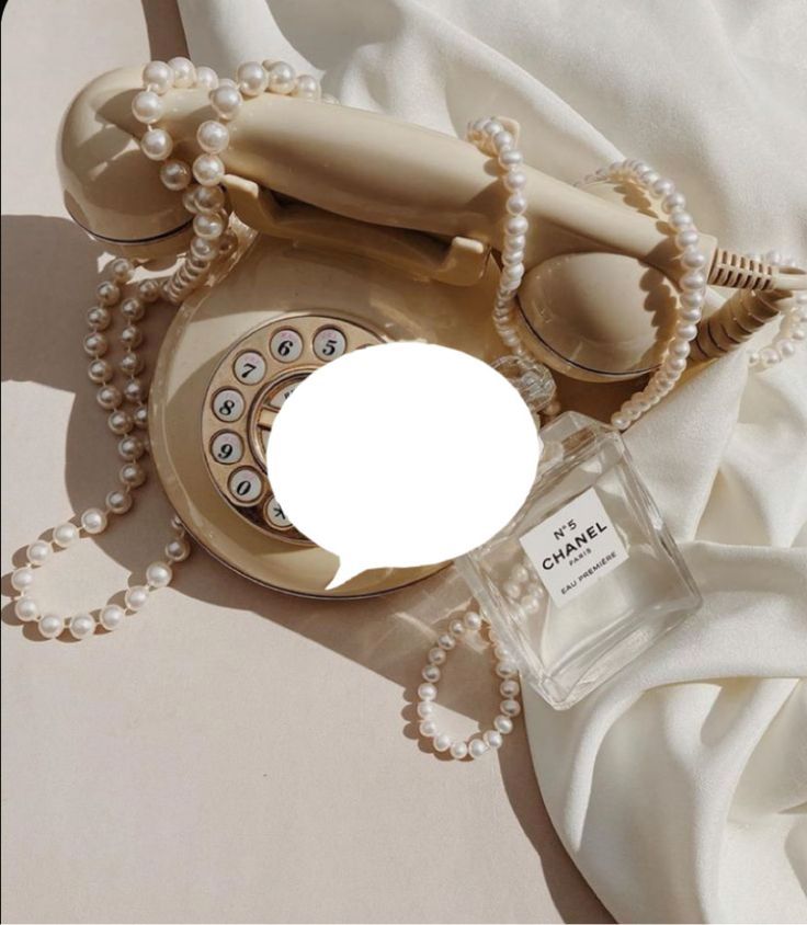 an old fashioned phone with pearls around it and a bottle of perfume next to it