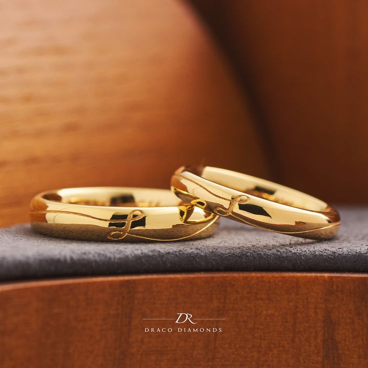 two gold wedding rings sitting on top of a wooden chair next to each other in front of a black cushion