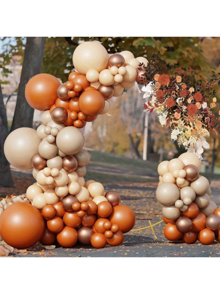 an arrangement of balloons and flowers on the ground in front of a tree with fall foliage