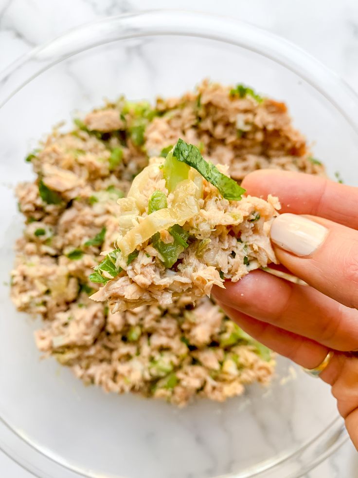 a hand holding a piece of food over a glass bowl filled with rice and broccoli