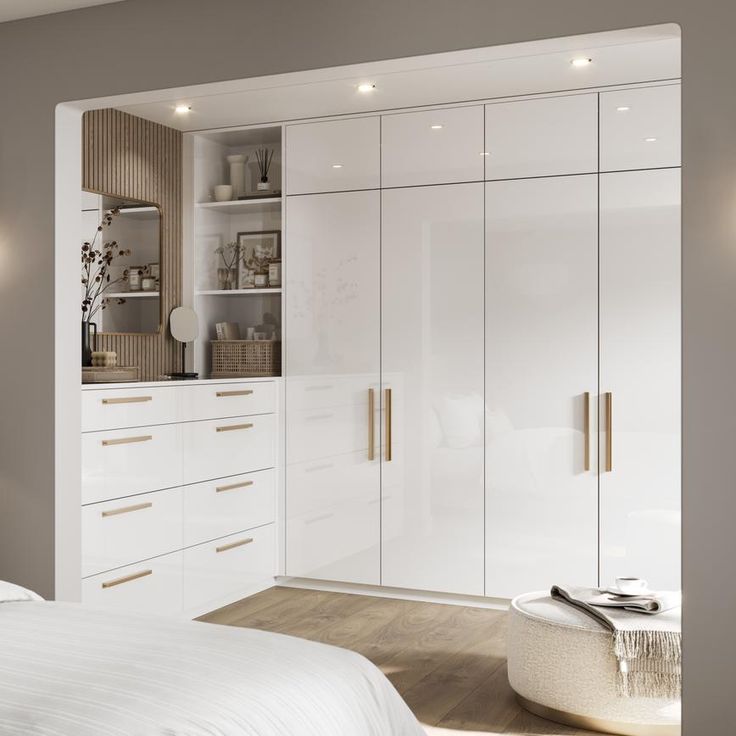 a bedroom with white cupboards and drawers next to a bed in front of a window