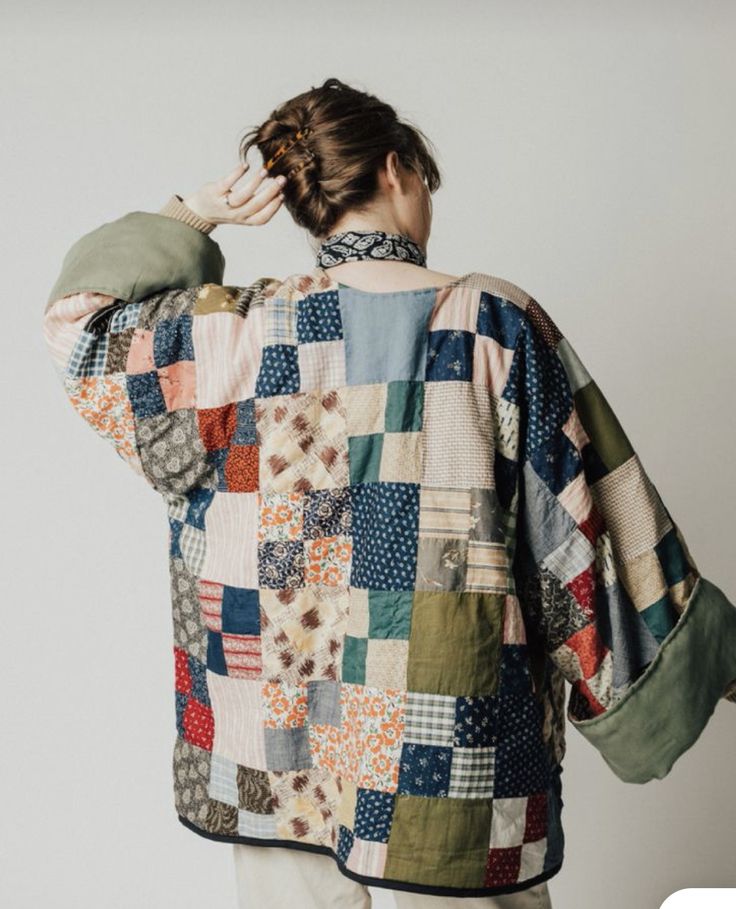 a woman wearing a multicolored patchwork jacket and white pants with her back to the camera