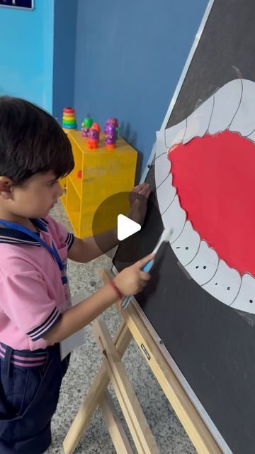 a little boy that is standing in front of a easel with a painting on it