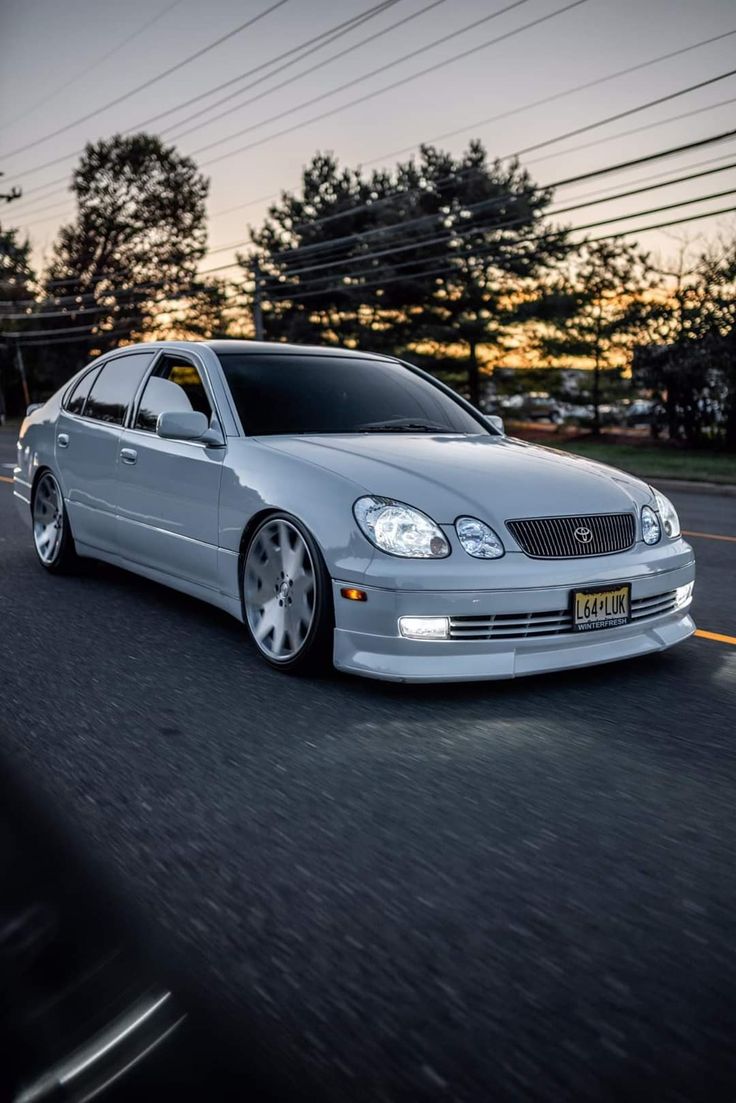 a silver car driving down the road at dusk with power lines in the back ground