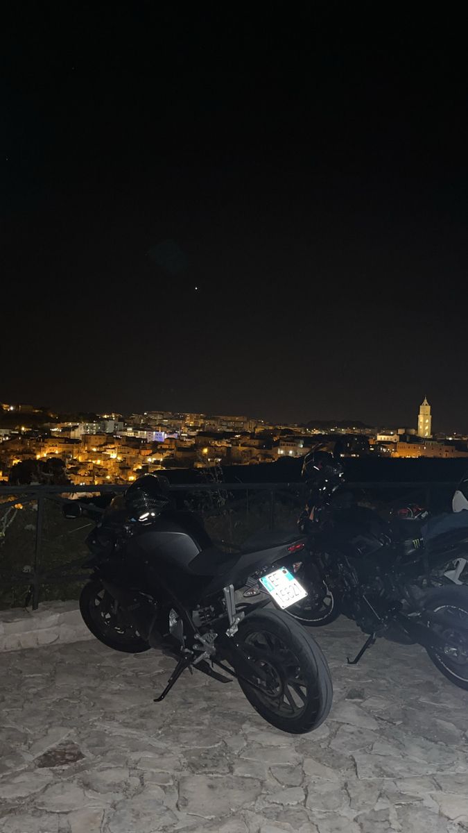 two motorcycles parked next to each other in front of a city skyline at night time