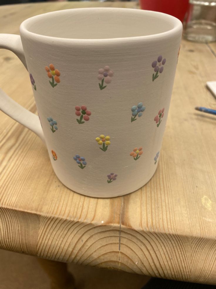 a white coffee cup sitting on top of a wooden table with flowers painted on it