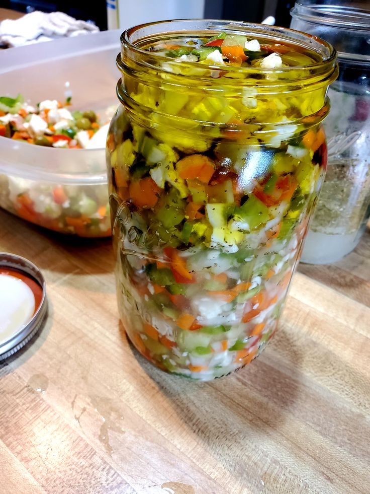 a mason jar filled with pickled vegetables on top of a wooden table next to other food