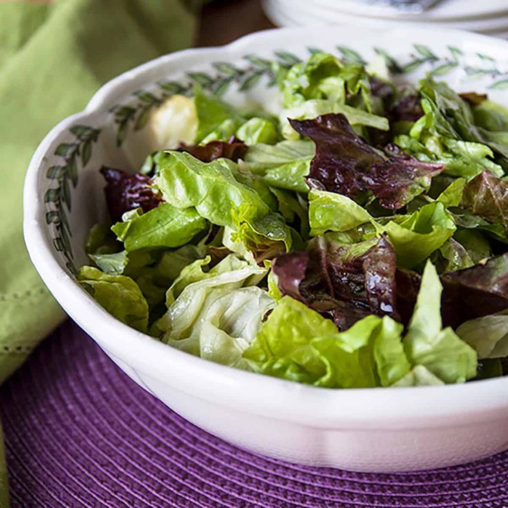 a white bowl filled with lettuce on top of a purple place mat