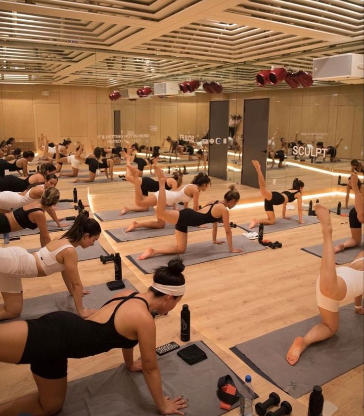 a large group of people doing yoga in a room with hard wood floors and ceilings