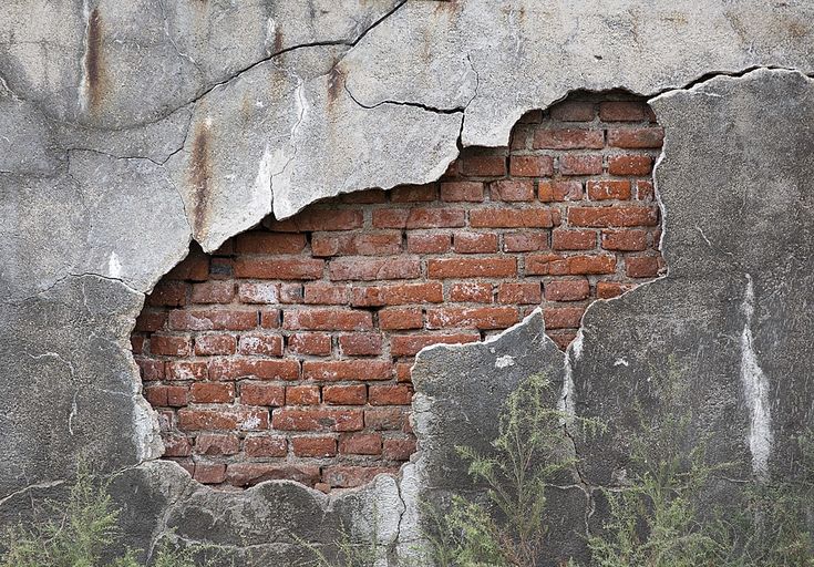 an old brick wall with a hole in the middle and weeds growing out of it