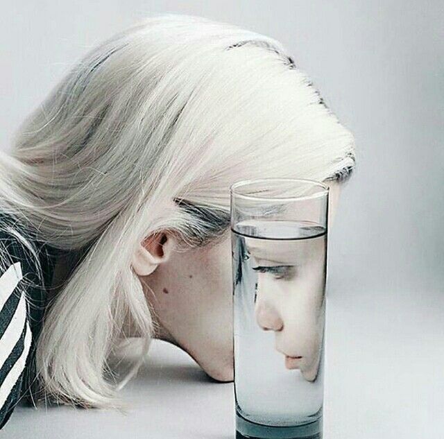 a woman with her head in a glass next to a drinking glass that is half empty