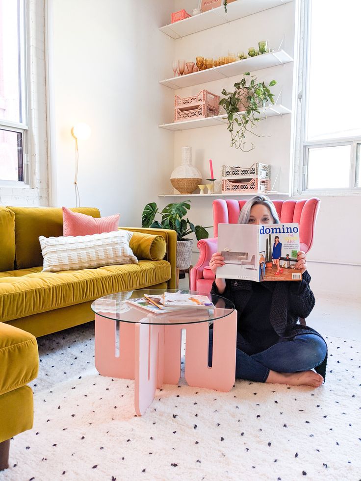 a woman sitting on the floor reading a magazine in front of a yellow couch and coffee table