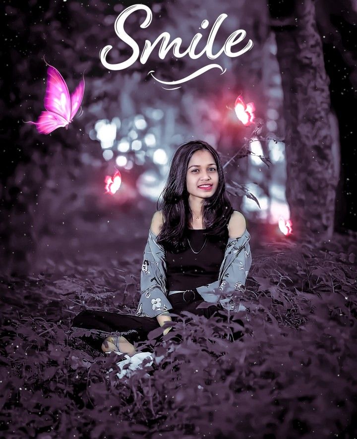 a woman sitting on the ground with a butterfly flying over her head and smiling at the camera