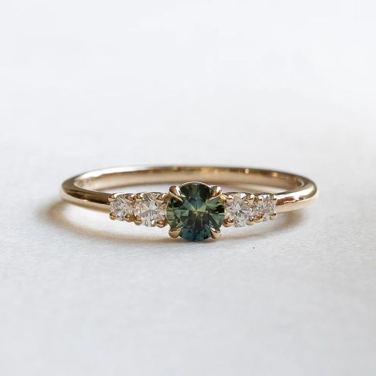 a green and white diamond ring sitting on top of a white surface with gold band