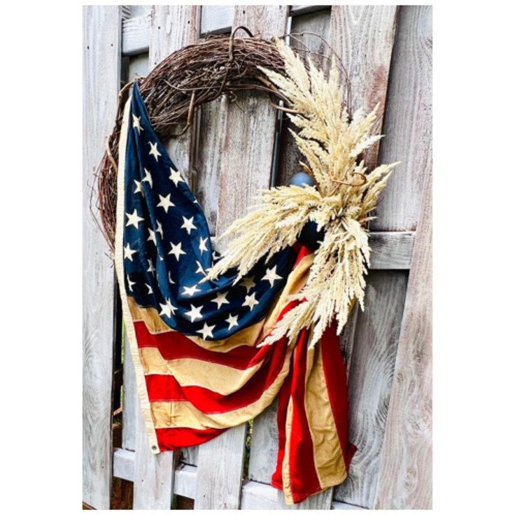 a wreath with an american flag on it is hanging on a wooden fence next to a wreath