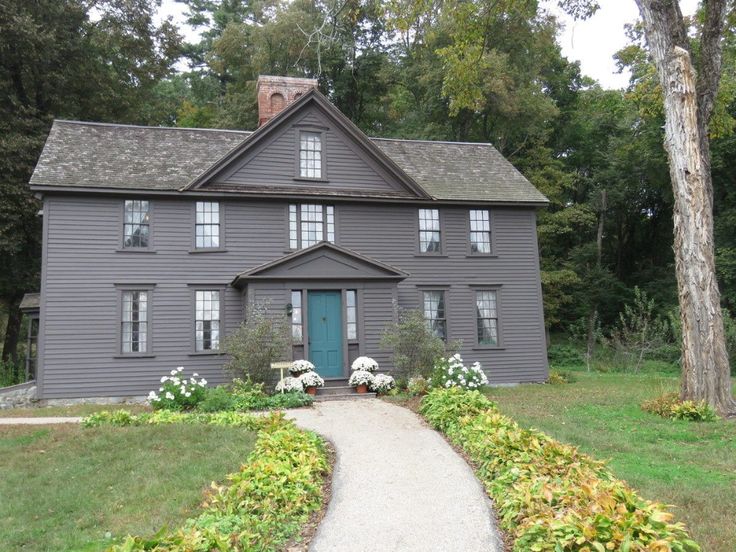 a gray house with white flowers and trees in the front yard, along with a path leading to it