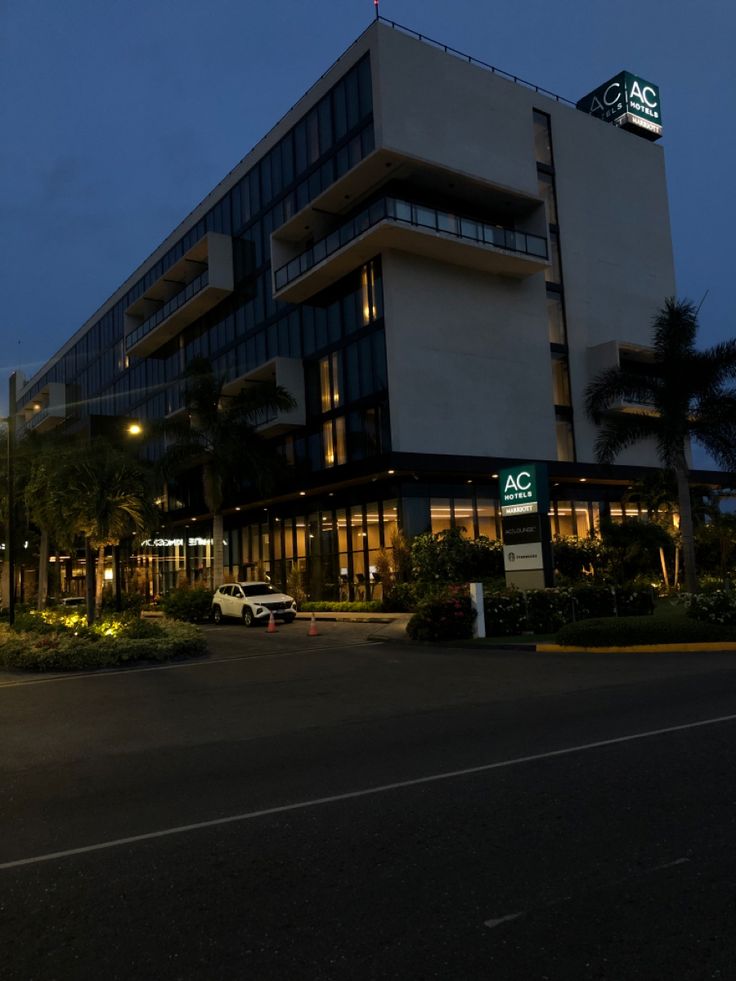 an office building lit up at night with palm trees in the foreground and cars parked on the street