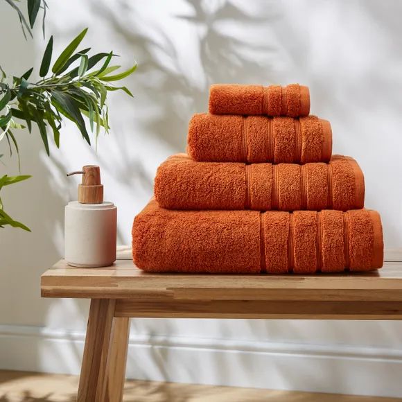 a stack of orange towels sitting on top of a wooden table next to a potted plant