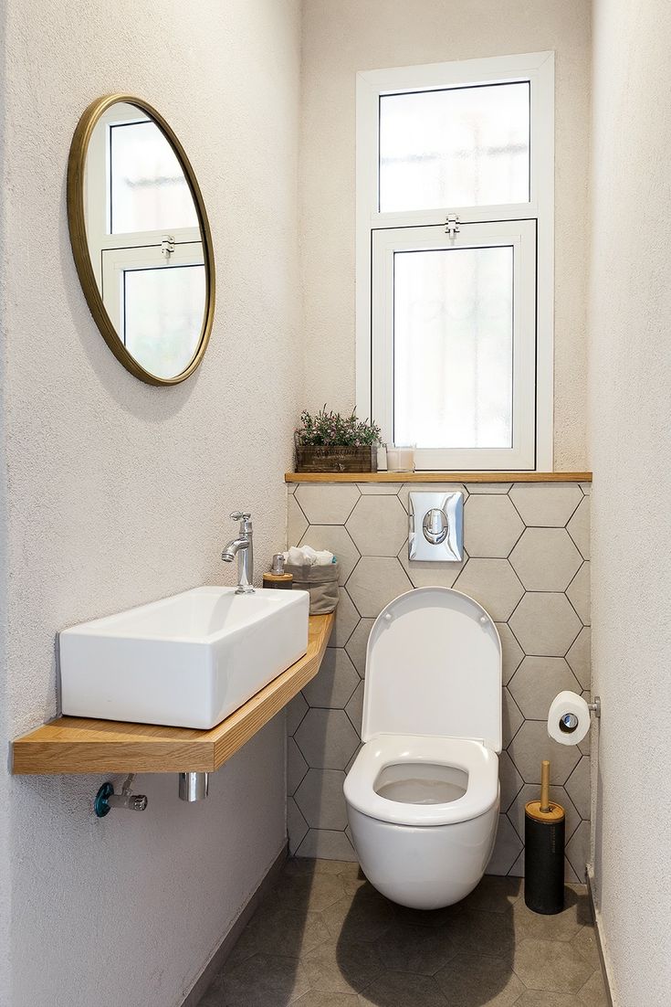 a white toilet sitting next to a sink in a bathroom under a round mirror on the wall