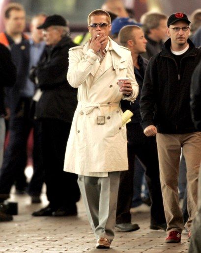 a man in a trench coat and sunglasses walking down the street with his hand on his face