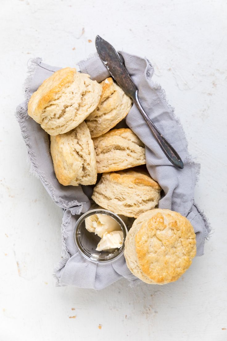 biscuits and butter on a cloth with a spoon next to it, sitting on a white surface