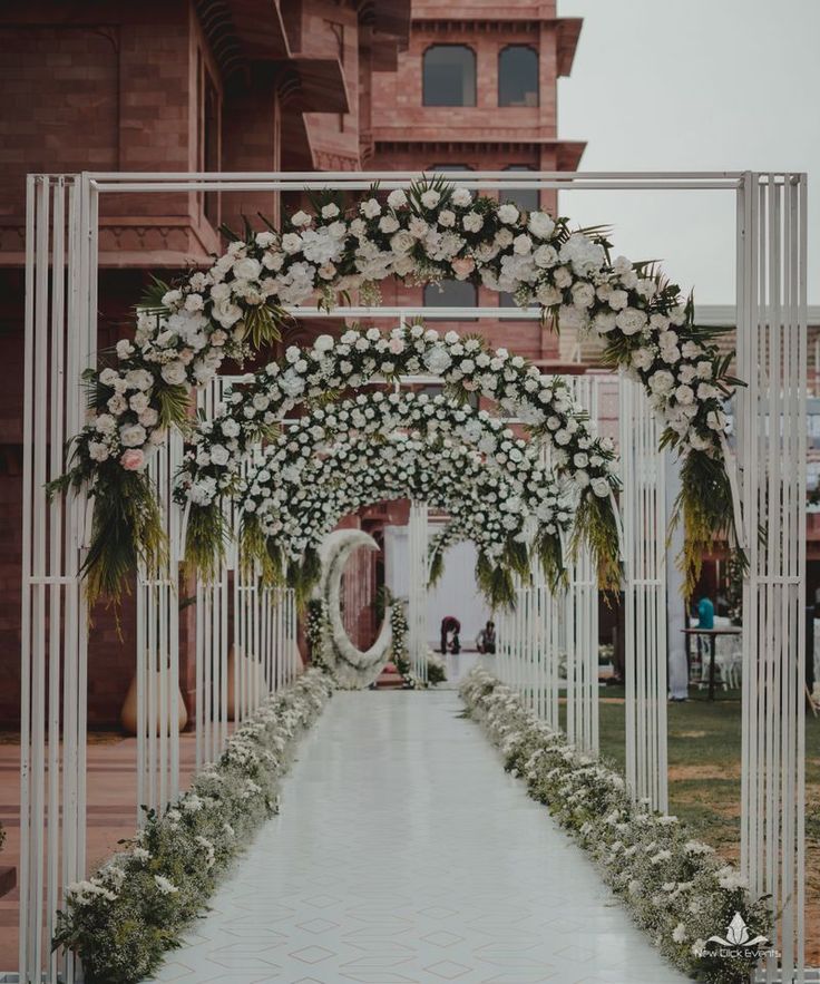 an archway decorated with white flowers and greenery for a wedding ceremony in front of a building