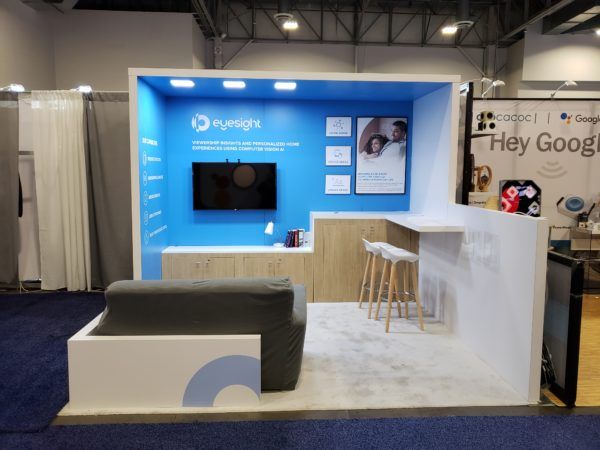 a trade show booth with blue walls and white carpeted flooring that has an area for stools to sit on