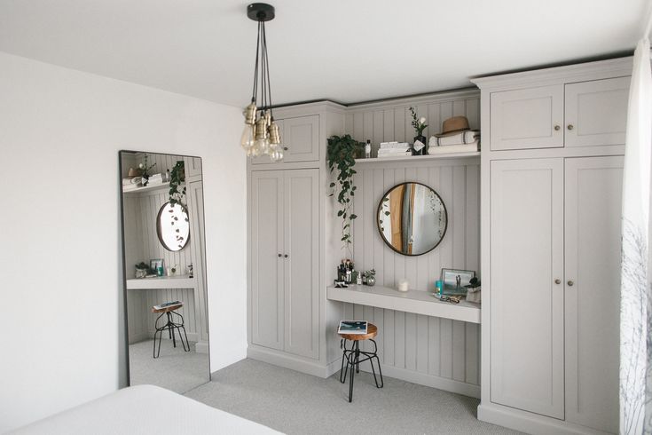 a bedroom with white walls and gray cupboards, mirrors on the wall, and a bed in front of it