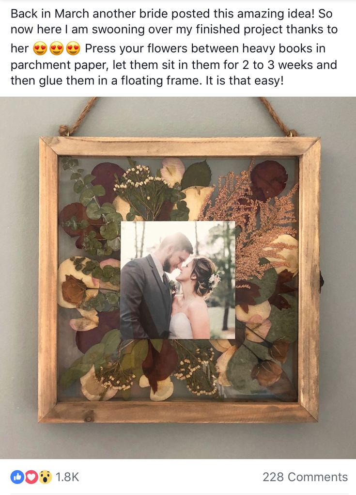 a wooden frame holding a photo of a bride and groom in front of leaves on the wall