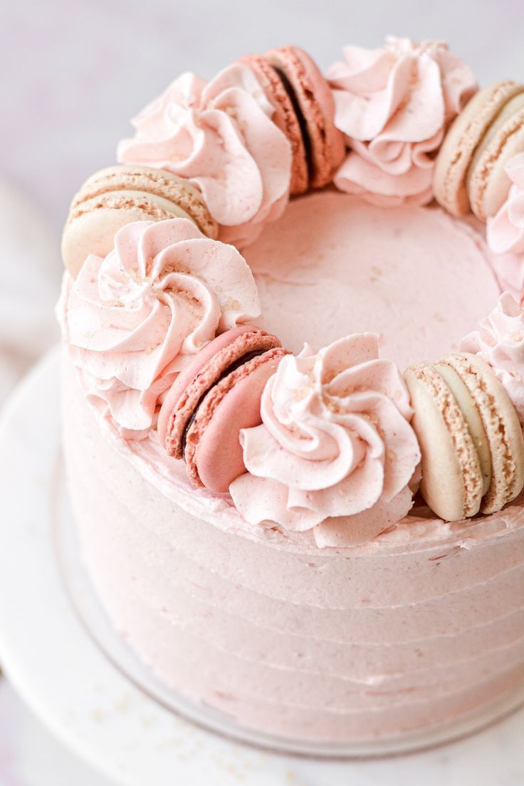 a pink frosted cake with macaroons and cookies on top, sitting on a white plate