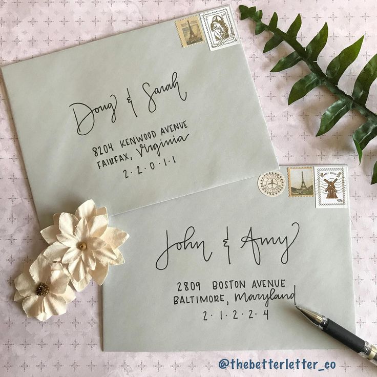 two envelopes with writing on them next to a pen and flower, which is also used as a postcard