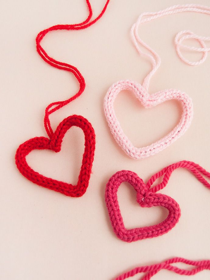 three crocheted hearts on a white surface with red and pink string attached to them