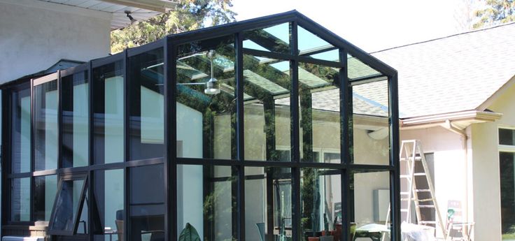 a glass house sitting in the middle of a yard next to a building with windows