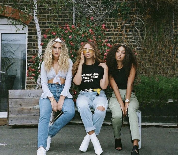 three women sitting on a bench in front of a brick wall