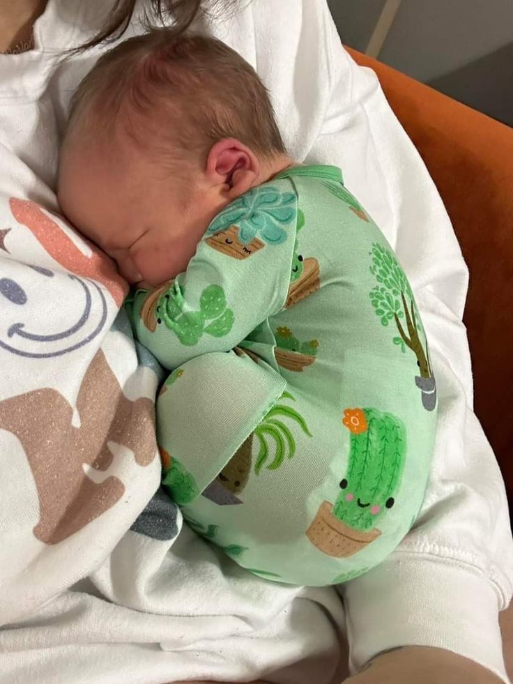 a baby sleeping on top of a blanket next to a woman's arm and head