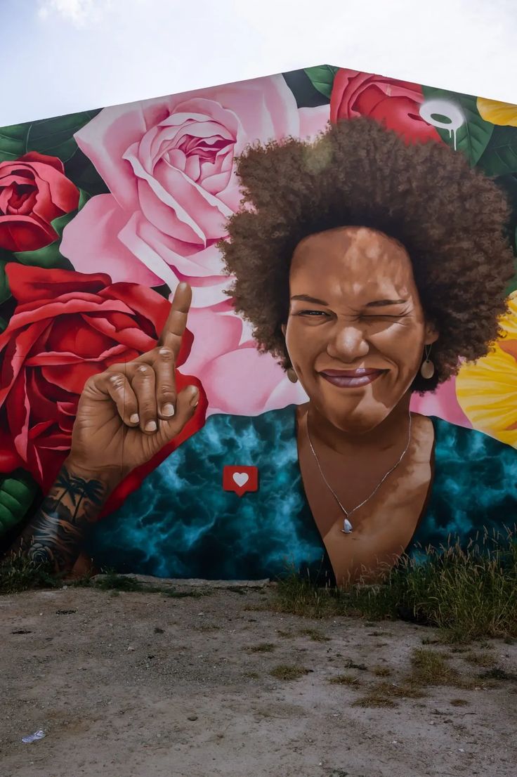 a woman with an afro pointing at the camera in front of a large flowered wall