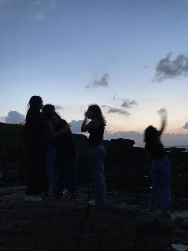 three women standing on top of a rocky hill at sunset with their arms in the air