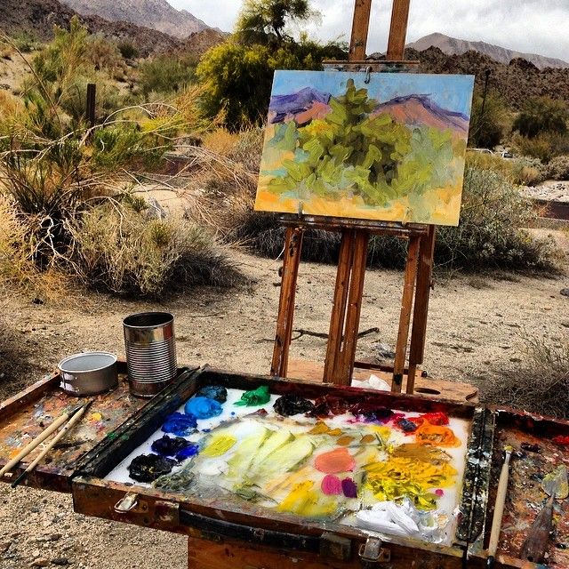 an artist's easel sitting in the desert with paint and brushes on it