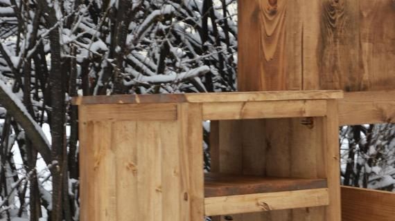 a wooden shelf sitting in front of some snow covered trees