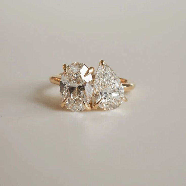 three pear shaped diamond engagement rings on a white surface with the top one in yellow gold