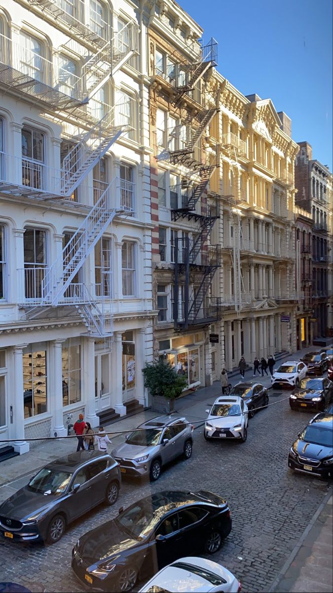 cars are parked on the street in front of tall buildings with balconies and fire escapes