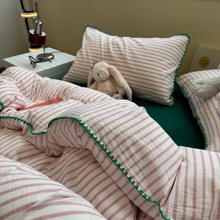 a bed with pink and white striped sheets, pillows and a stuffed animal on it